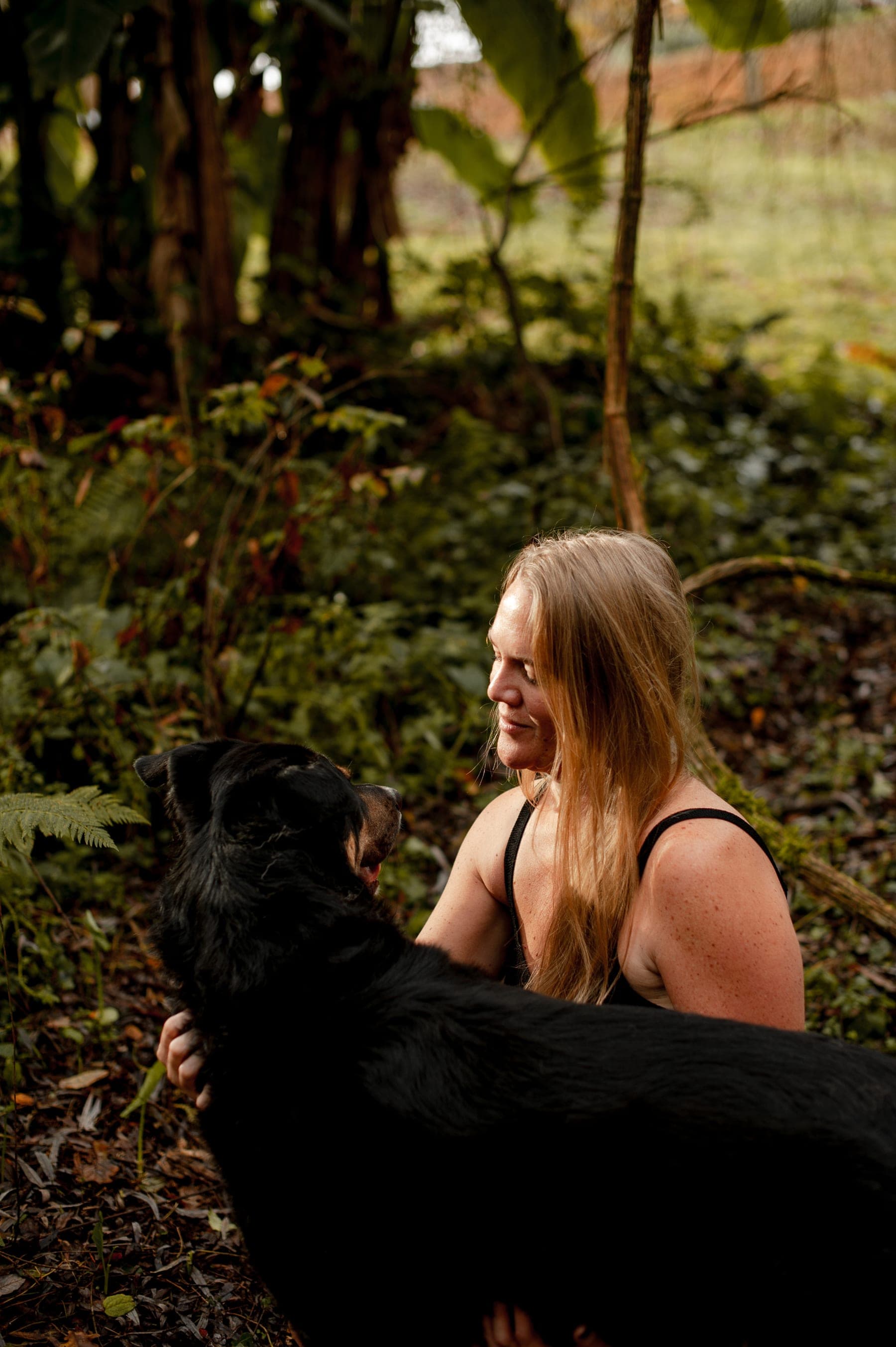 Léa en échange rapproché avec un chien noir, au pied d'un arbre